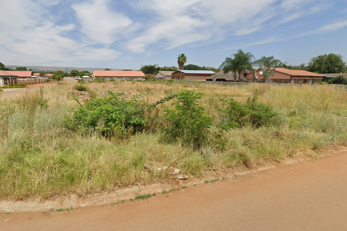 A vacant residential corner plot featuring established road access and kerbing, situated in a developed suburban neighborhood.
