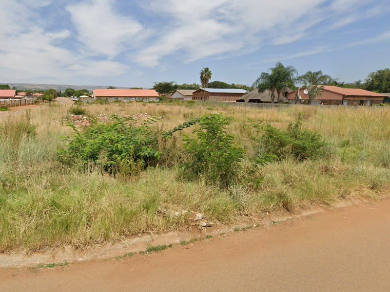 A vacant residential corner plot featuring established road access and kerbing, situated in a developed suburban neighborhood.