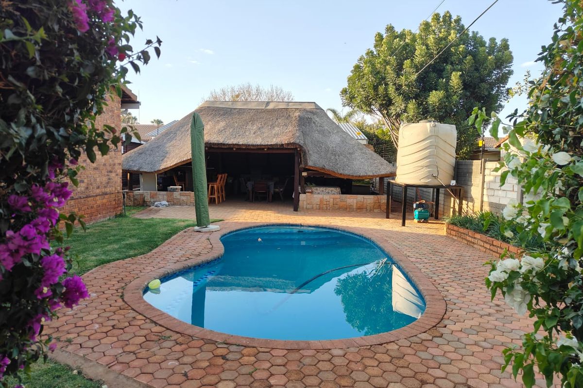 Outdoor pool area featuring a kidney-shaped swimming pool, brick paving, and a covered thatched lapa entertainment space.