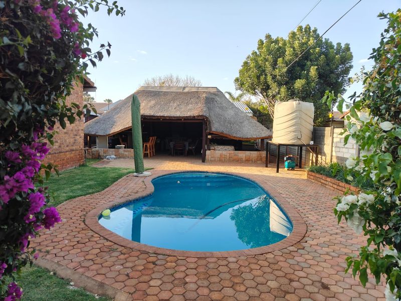 Outdoor pool area featuring a kidney-shaped swimming pool, brick paving, and a covered thatched lapa entertainment space.