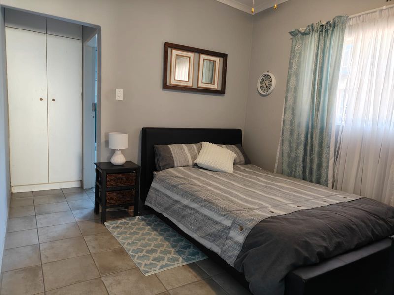 A functional bedroom featuring neutral wall tones, tiled flooring, and built-in cupboard storage.