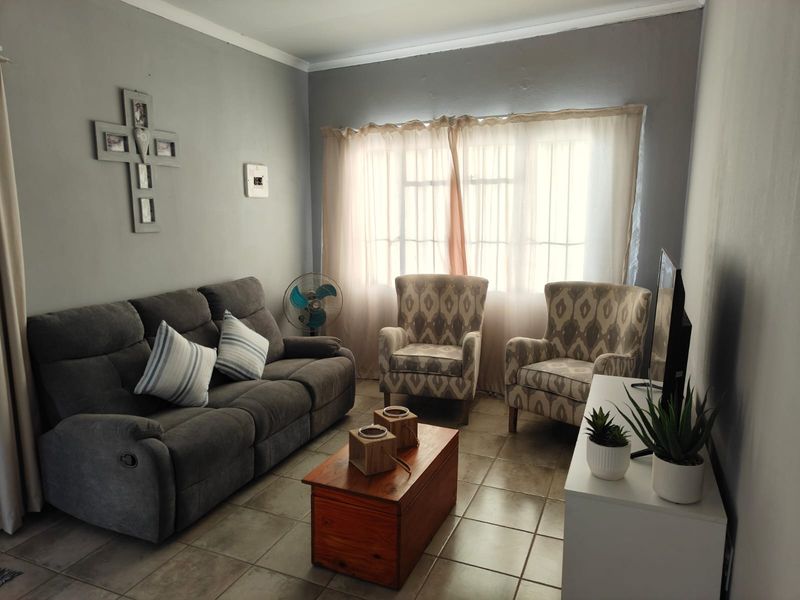A comfortable living room featuring tiled flooring and natural light through a large window with curtain rails.