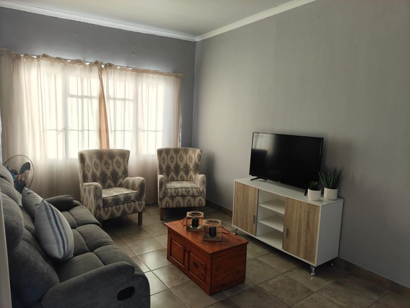 A comfortable living room featuring neutral grey walls and tiled flooring, providing a functional and well-lit space for relaxation.