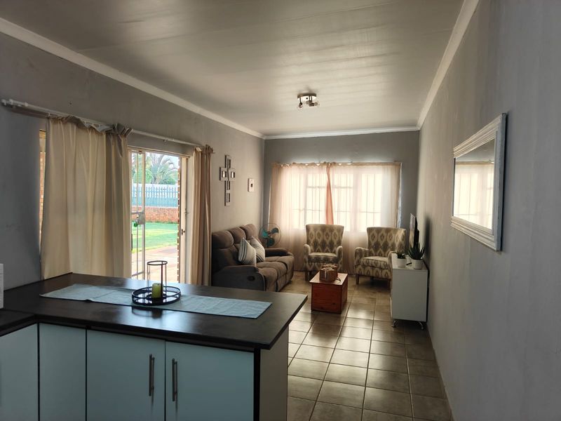 Open-plan living area featuring tiled flooring, kitchen cabinetry with a dark countertop, and a sliding glass door providing access to the garden.