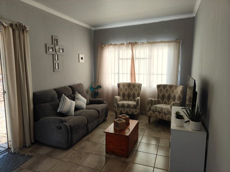 A comfortable living room featuring tiled flooring, neutral wall tones, and a sliding door providing access to the exterior.