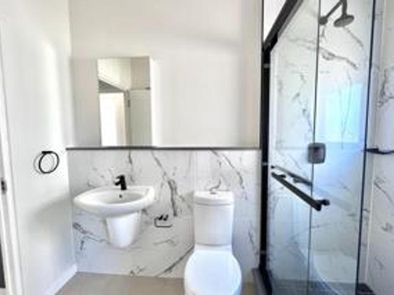 Modern bathroom featuring marble-look wall tiles, a wall-mounted basin, a toilet, and a glass-enclosed shower with contemporary black tapware.