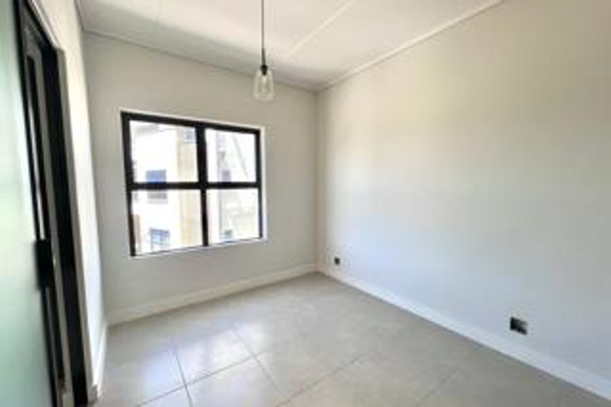 A bright, empty bedroom featuring neutral tiled flooring, clean white walls, and a modern pendant light fixture.