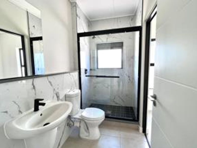 Modern bathroom featuring marble-look wall tiles, a walk-in shower with a black frame, a pedestal basin with a black mixer tap, and a toilet.