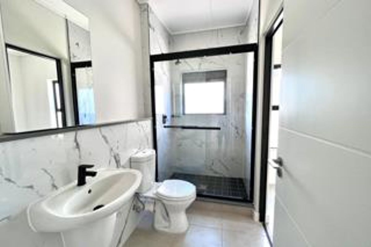 Modern bathroom featuring marble-look wall tiles, a walk-in shower with a black frame, a pedestal basin with a black mixer tap, and a toilet.