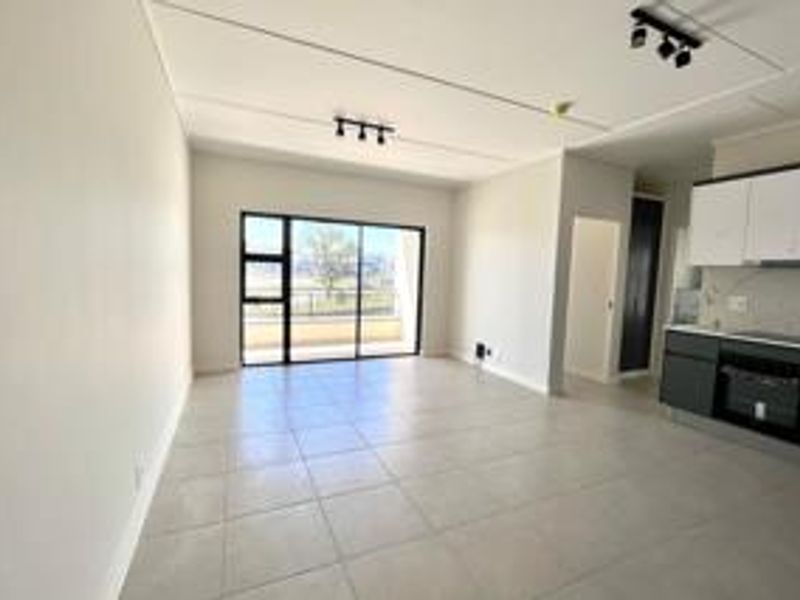 Spacious open-plan living area featuring tiled floors, modern kitchen cabinetry with built-in appliances, and large sliding doors leading to an outdoor balcony.