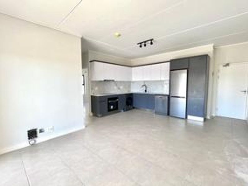 Modern open-plan living area featuring a sleek kitchen with two-tone cabinetry, integrated appliances, and neutral tiled flooring throughout.