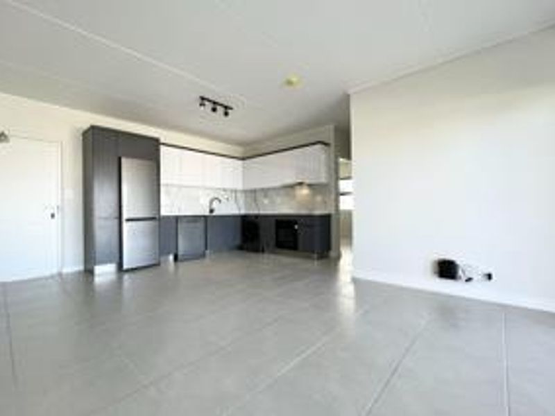 Modern open-plan kitchen and living area featuring sleek two-tone cabinetry, integrated appliances, marble-look splashback, and neutral tiled flooring throughout.