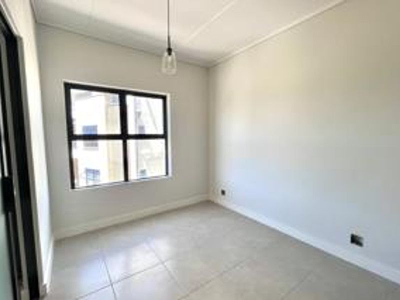 A bright, empty bedroom featuring neutral tiled flooring, clean white walls, and a modern pendant light fixture.