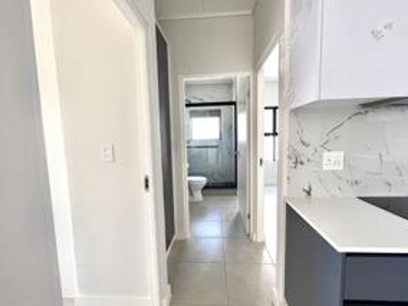 A modern hallway view featuring sleek cabinetry, marble-look backsplash, and quartz countertops, leading towards a bathroom and bedroom area.