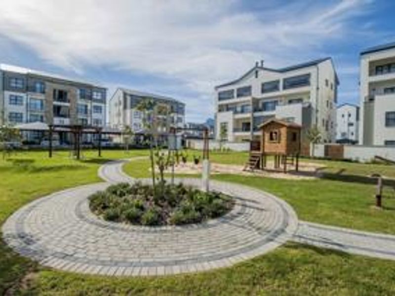 Well-maintained communal garden area featuring paved walkways, landscaped greenery, and a children's play structure within a modern apartment complex.
