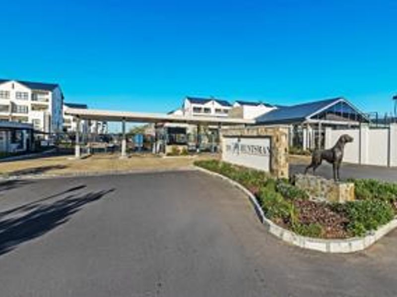 The entrance to The Huntsman apartment complex, featuring a secure gatehouse, paved driveway, and landscaped signage area.