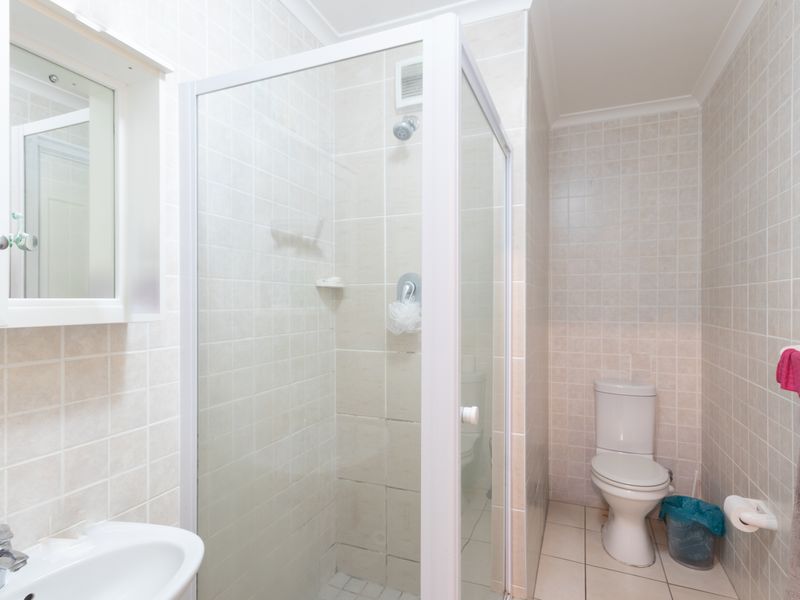 A functional bathroom featuring a glass-enclosed shower, a standard toilet, and a wall-mounted vanity basin with a mirrored medicine cabinet.