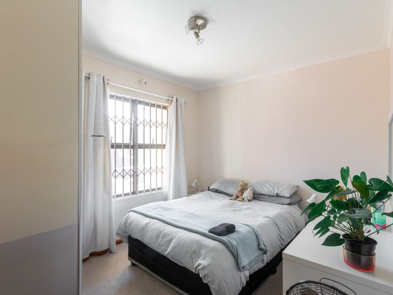 A standard bedroom featuring a window with a security gate and neutral wall finishes.