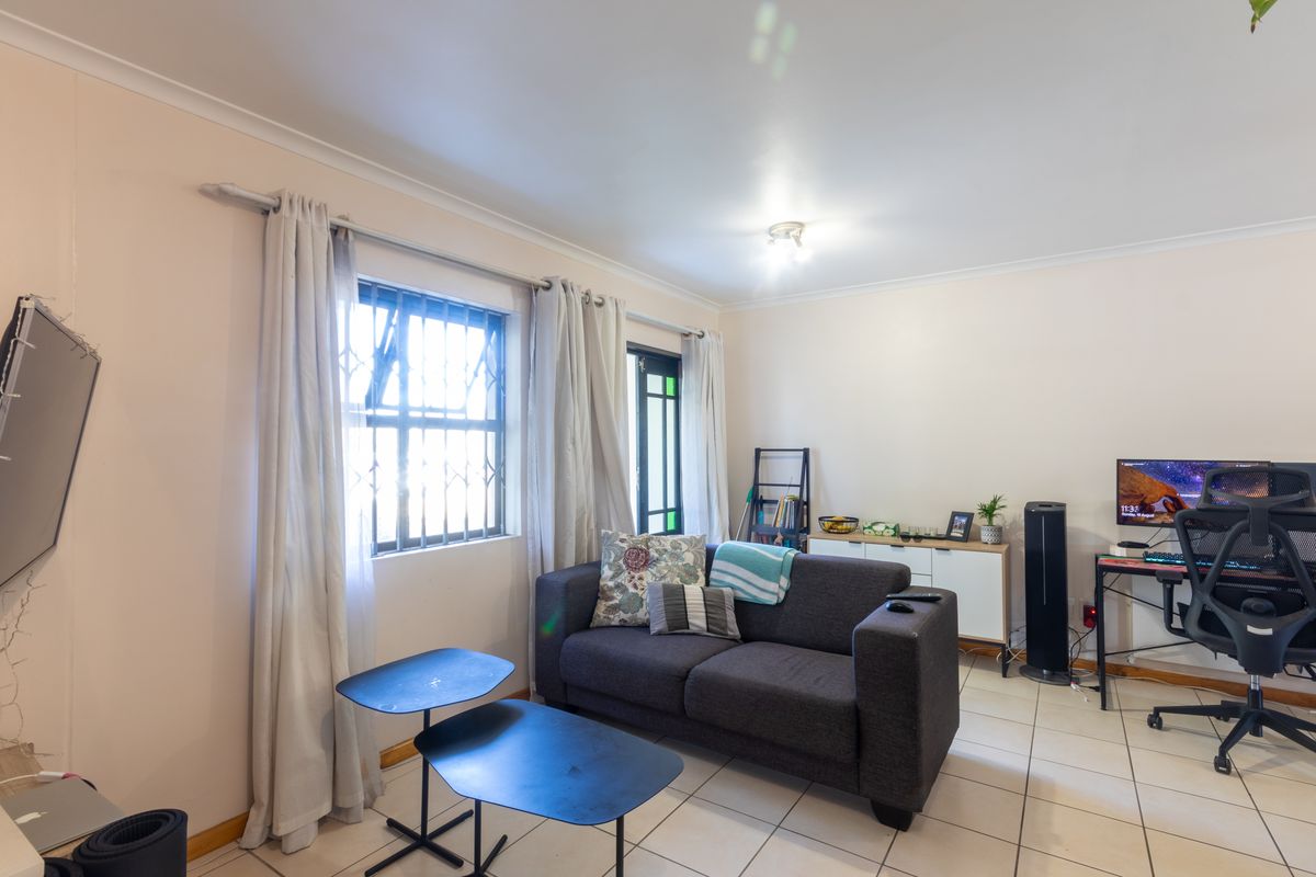 A functional living room featuring tiled flooring, security bars on the window, and a glass panel door, providing a practical and well-lit living space.