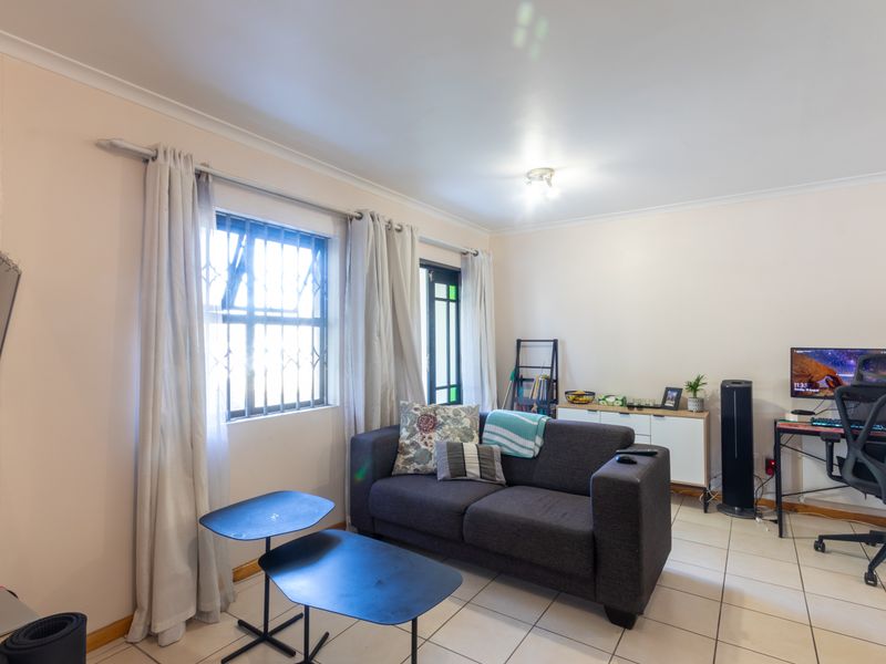 A functional living room featuring tiled flooring, security bars on the window, and a glass panel door, providing a practical and well-lit living space.