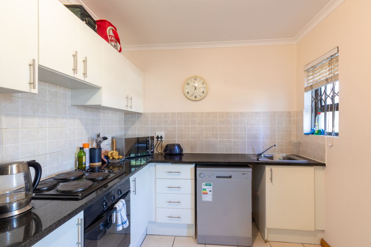 A functional kitchen featuring white cabinetry, dark granite countertops, tiled backsplash, integrated electric hob, oven, and a window with a security gate.