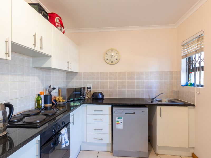 A functional kitchen featuring white cabinetry, dark granite countertops, tiled backsplash, integrated electric hob, oven, and a window with a security gate.