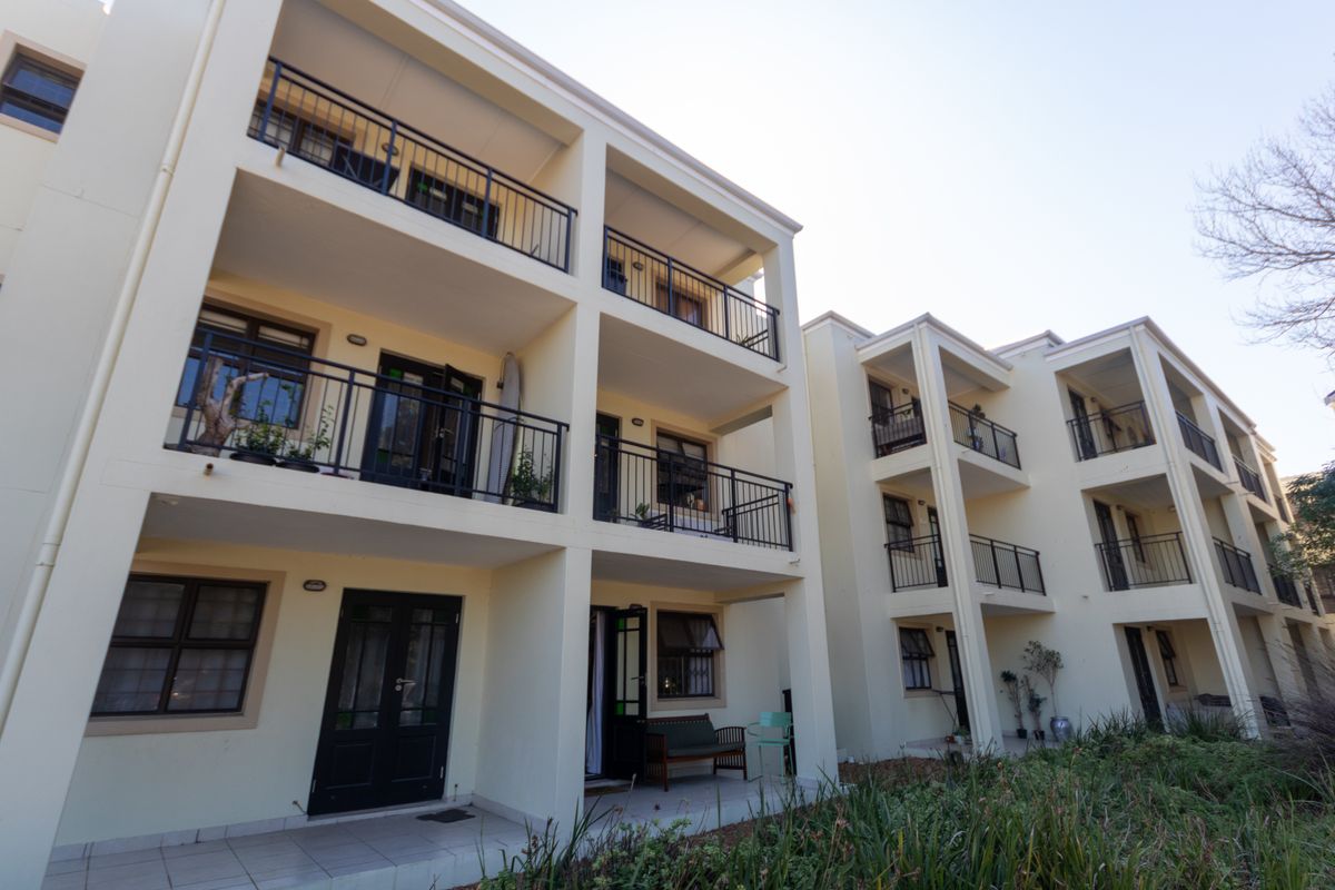 Rear elevation of a multi-story apartment complex featuring private balconies with metal railings and ground-floor patio access.