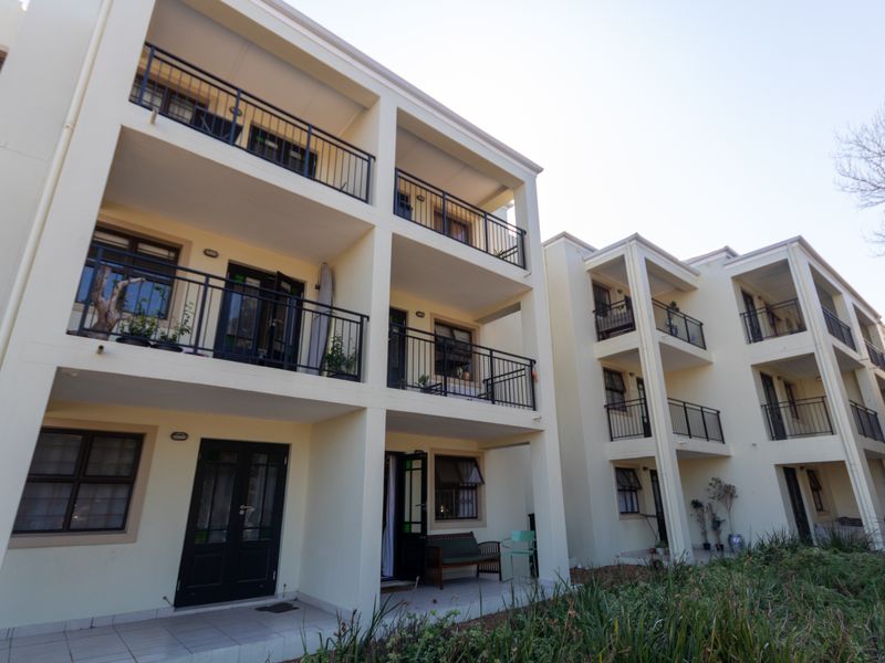 Rear elevation of a multi-story apartment complex featuring private balconies with metal railings and ground-floor patio access.