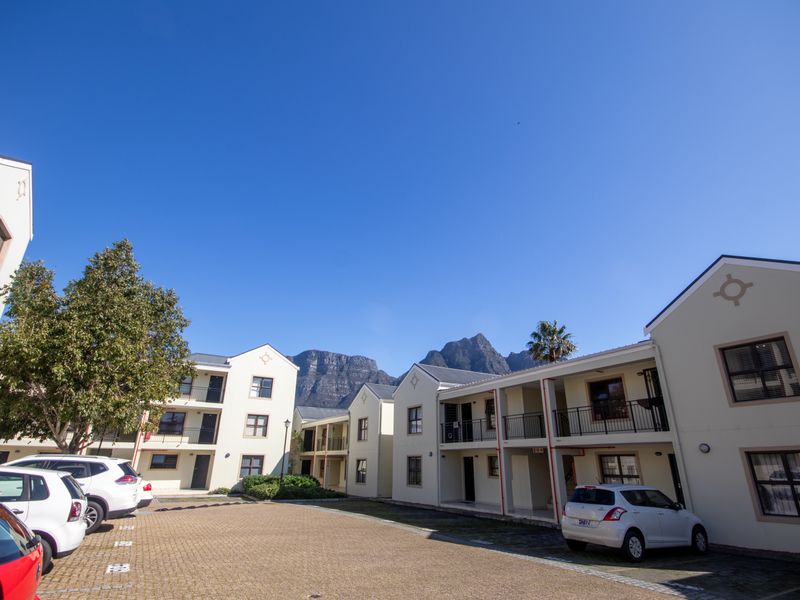 Exterior view of a multi-story apartment complex featuring paved parking, balconies, and mountain views in the background.