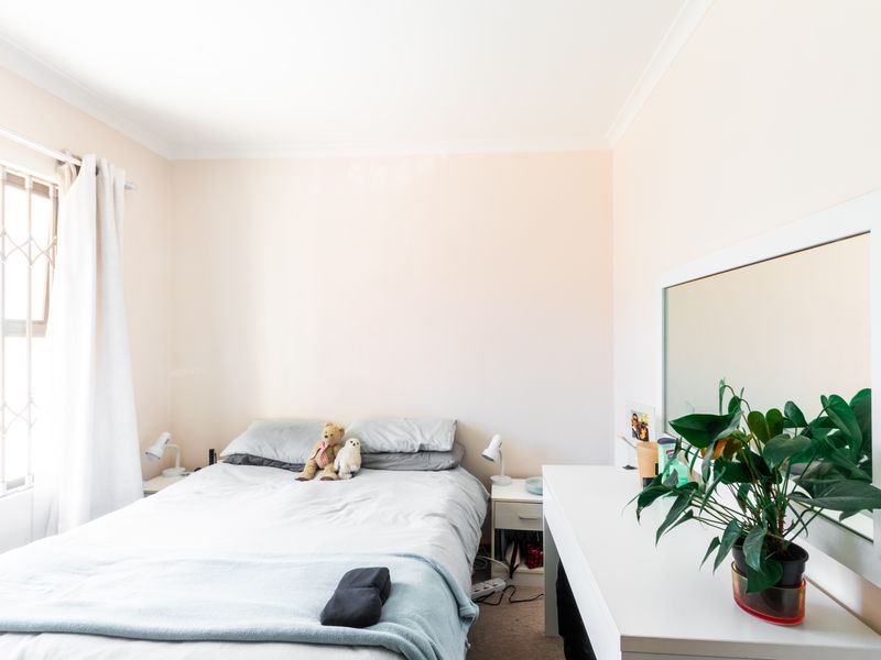 A well-lit bedroom featuring neutral wall finishes, carpeted flooring, and security bars on the window.