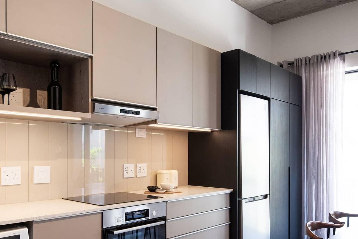 Modern kitchen featuring sleek handleless cabinetry, stone countertops, glass splashback, integrated appliances, and a striking exposed concrete ceiling.