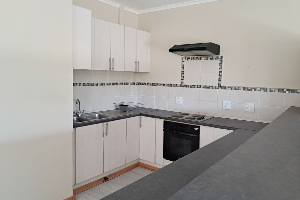 A functional kitchen featuring light-toned cabinetry, dark countertops, a built-in oven with hob, and a breakfast bar, offering a clean and practical layout.