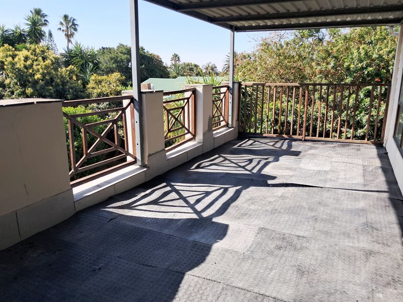 A spacious covered balcony featuring a timber balustrade and rubber flooring, offering an outdoor area with potential for refurbishment.