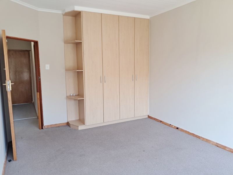 A vacant bedroom featuring neutral walls, carpeted flooring, and ample built-in cupboard storage with integrated shelving.