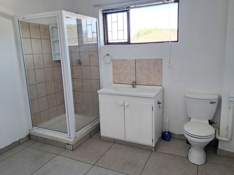 A functional bathroom featuring a shower enclosure, vanity cabinet with basin, and toilet, finished with tiled flooring and a window with security bars.