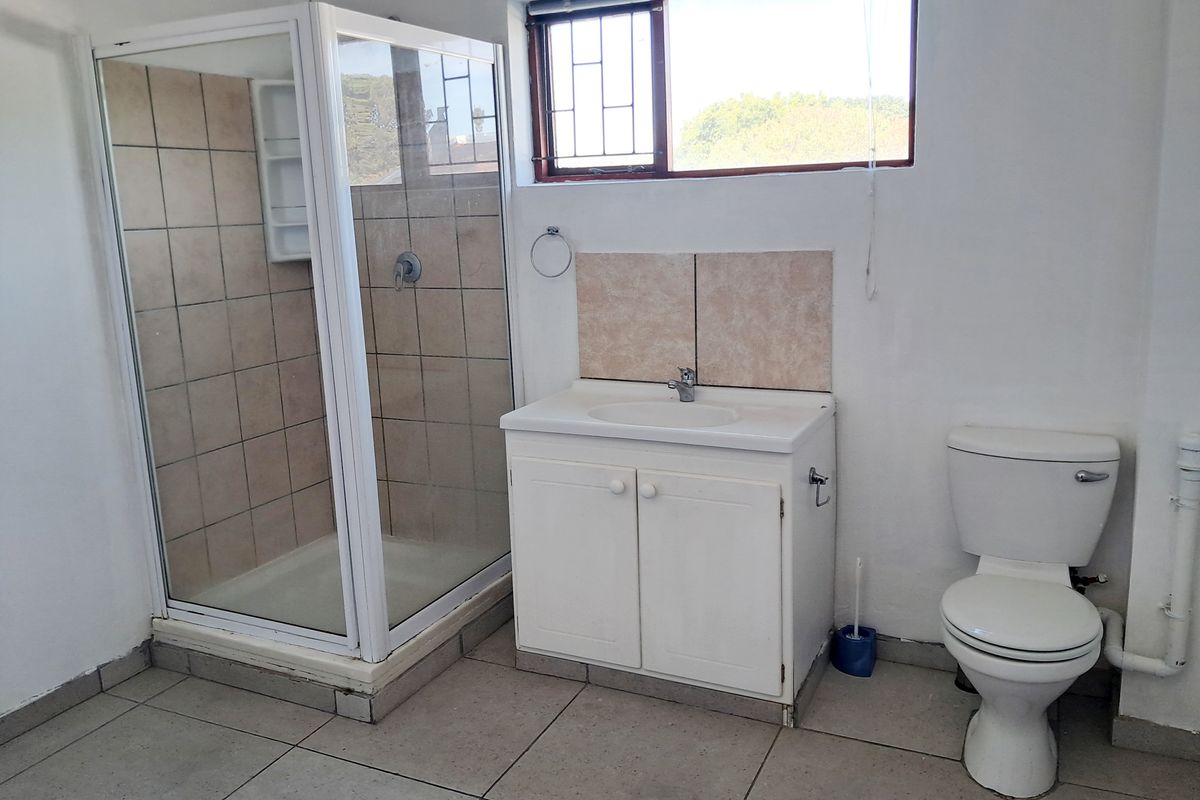 A functional bathroom featuring a shower enclosure, vanity cabinet with basin, and toilet, finished with tiled flooring and a window with security bars.
