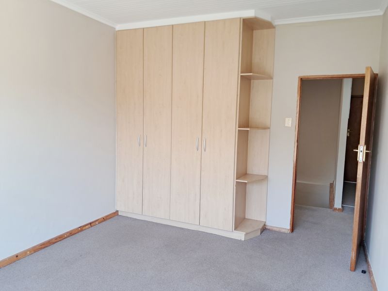 A vacant bedroom featuring light-toned built-in cupboards with integrated shelving and neutral carpeting.