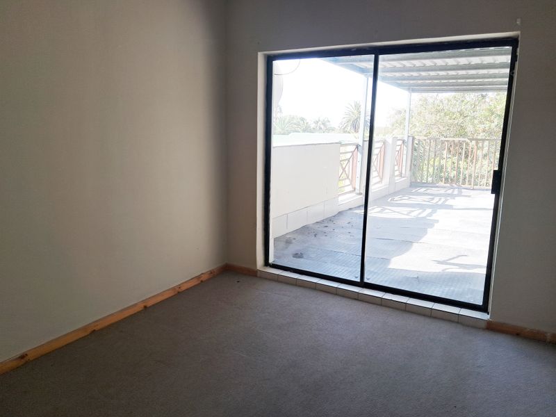 An empty bedroom featuring carpet flooring and a large sliding glass door providing access to an outdoor balcony area.