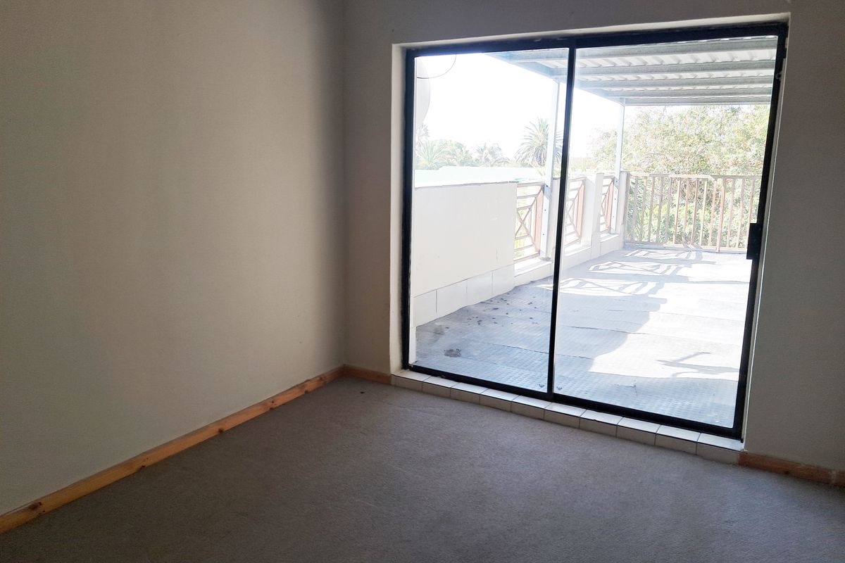 An empty bedroom featuring carpet flooring and a large sliding glass door providing access to an outdoor balcony area.