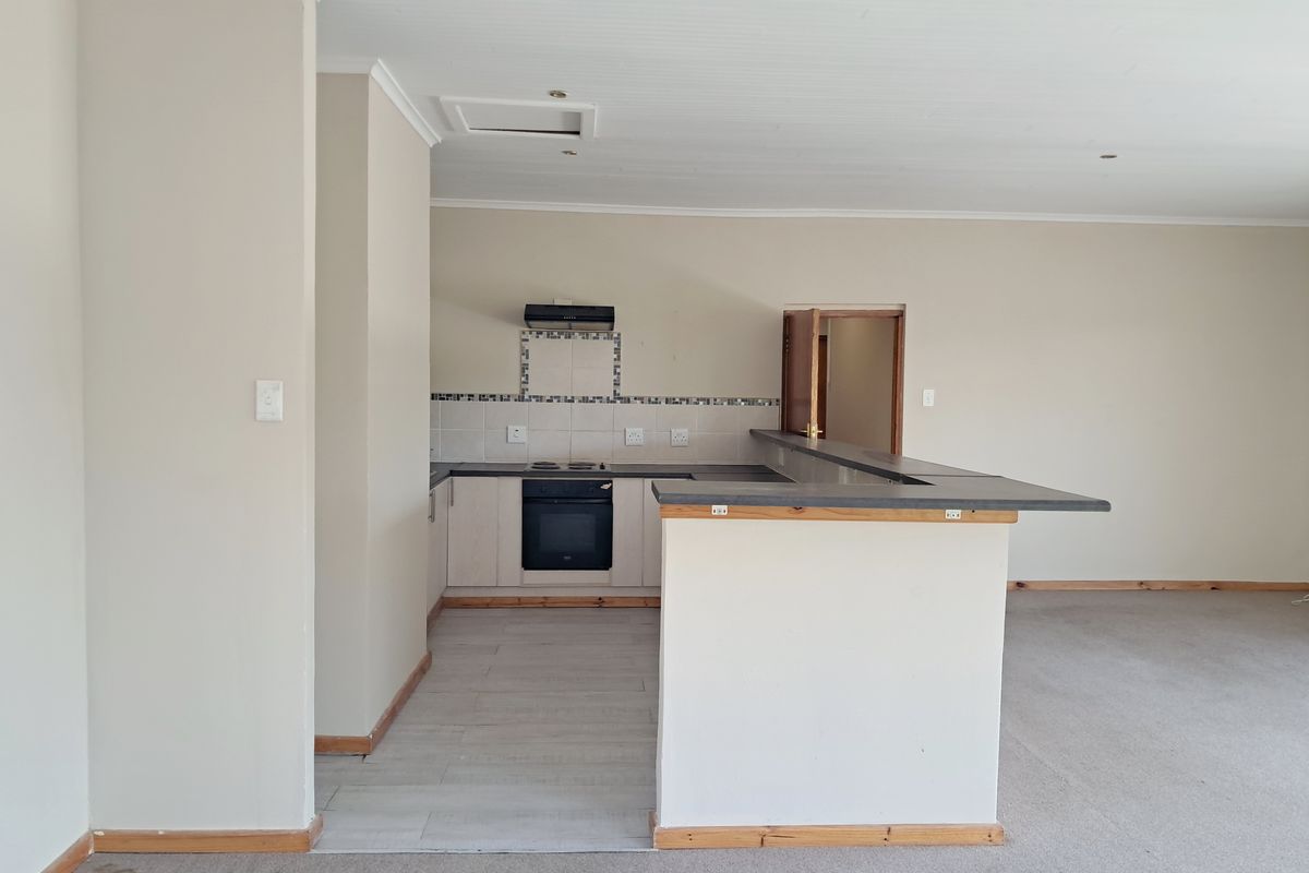 An open-plan kitchen and living area featuring a breakfast bar, built-in oven, hob, and extractor fan, with neutral finishes throughout.