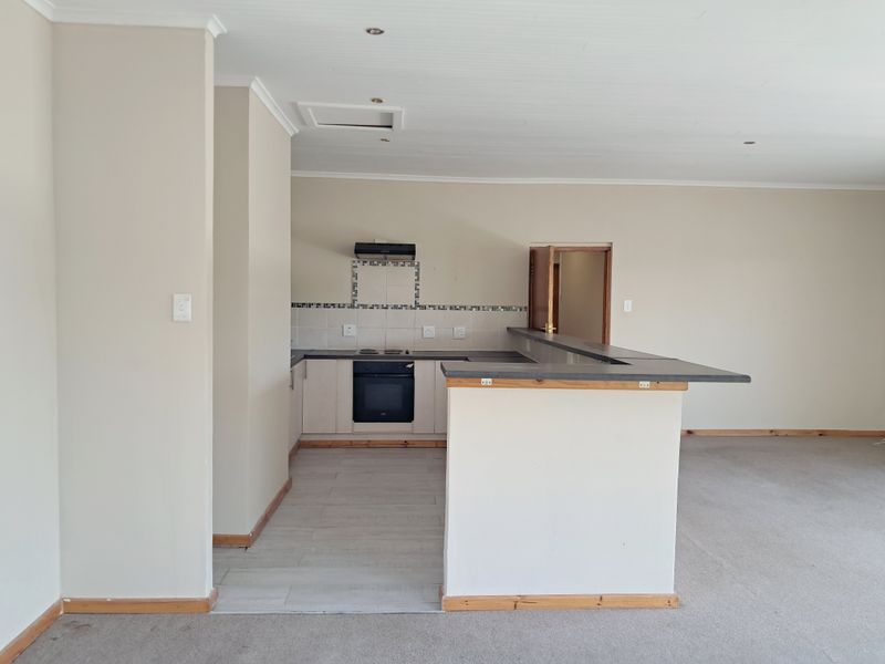 An open-plan kitchen and living area featuring a breakfast bar, built-in oven, hob, and extractor fan, with neutral finishes throughout.