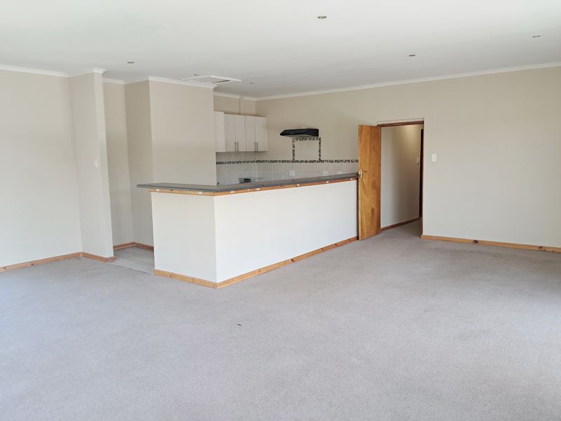 Spacious open-plan living area featuring a kitchen with breakfast bar, built-in cabinetry, and neutral finishes, offering a versatile layout for modern living.