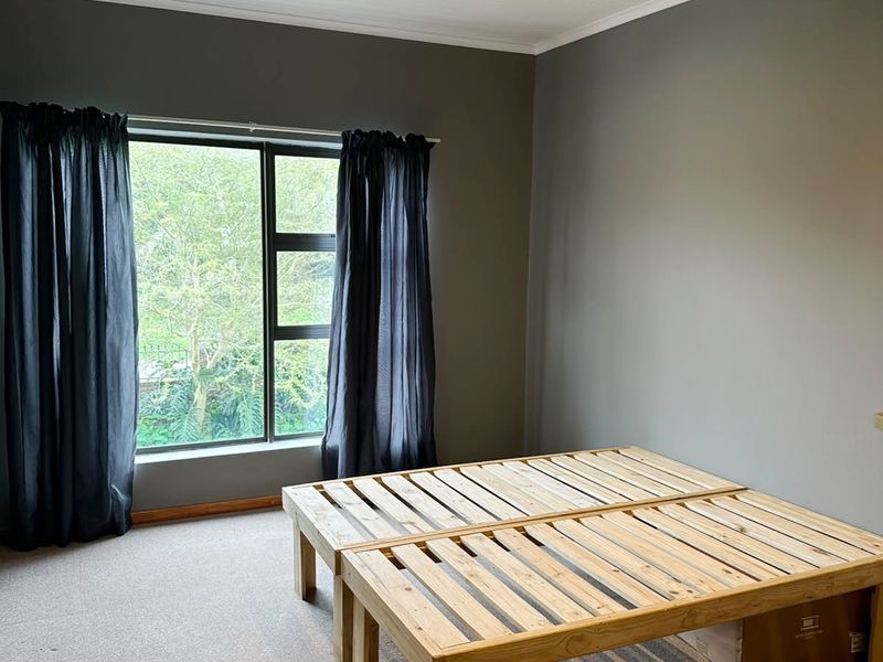 A spacious bedroom featuring neutral grey walls, carpeted flooring, and a tongue and groove ceiling with recessed lighting.