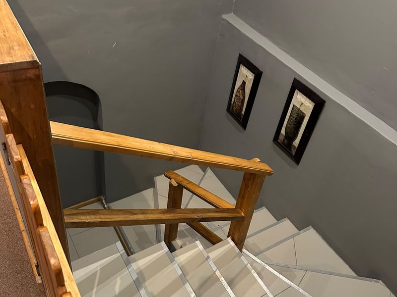 A staircase featuring tiled treads and a wooden handrail, leading to a lower level with grey painted walls.