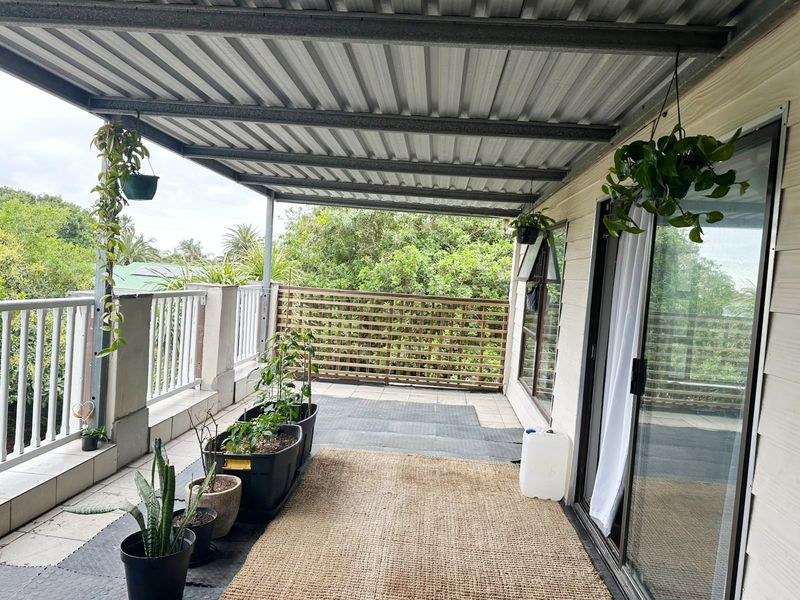 A covered balcony featuring a corrugated metal roof, tiled flooring, and a timber privacy screen, offering a functional outdoor living space.