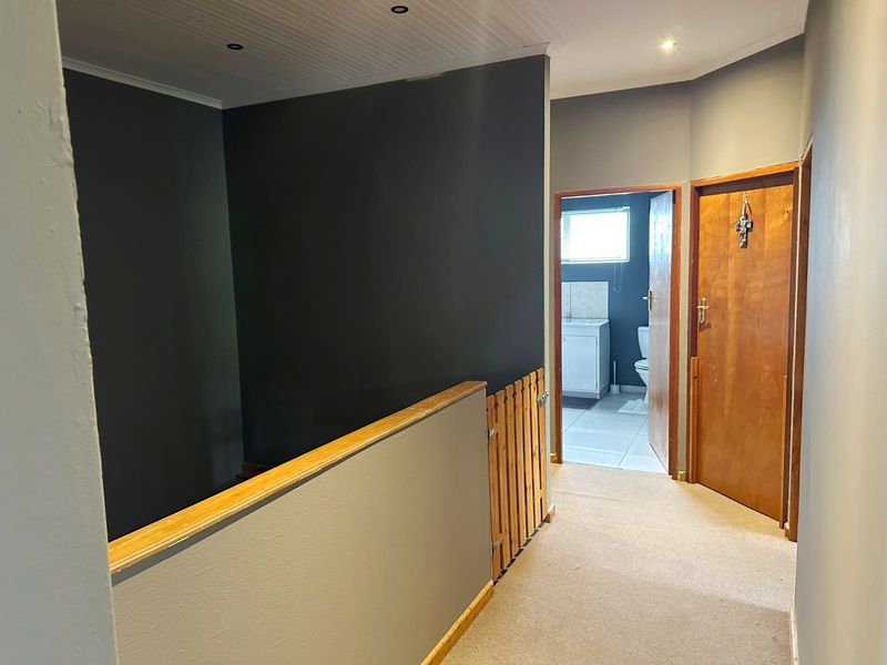 A carpeted hallway featuring a timber balustrade, tongue and groove ceiling, and access to an adjacent bathroom.