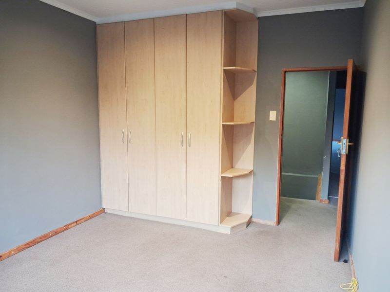 A bedroom featuring light wood-toned built-in wardrobes with integrated shelving, grey walls, and carpet flooring.