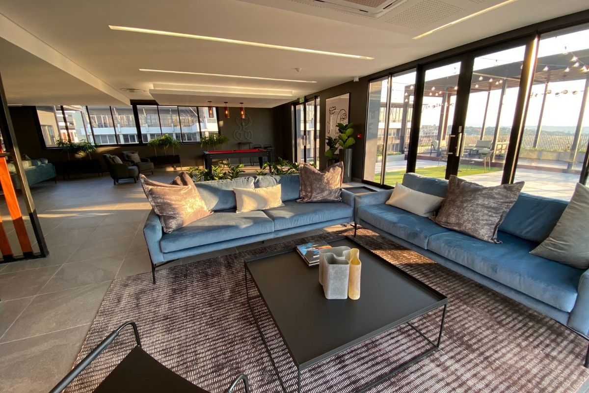 Spacious modern living area featuring large format floor tiles, recessed ceiling lighting, ducted air conditioning, and expansive floor-to-ceiling glass doors opening to a terrace.