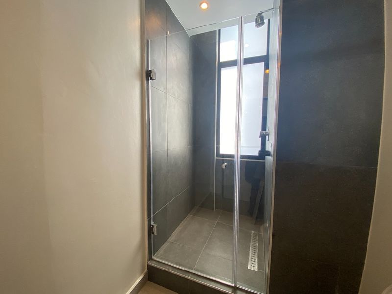 A modern walk-in shower featuring dark grey wall tiles, a glass enclosure, and a linear floor drain.