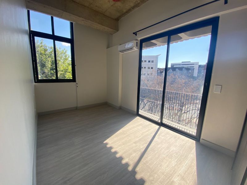 Bright and modern bedroom featuring exposed concrete ceilings, laminate flooring, a split-system air conditioner, and sliding glass doors leading to a balcony.